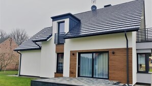 Uma casa moderna de dois andares com telhado plano, grandes portas de vidro deslizantes e uma pequena varanda.