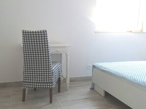 Een slaapkamer met een bed, een stoel, een bureau en een raam.