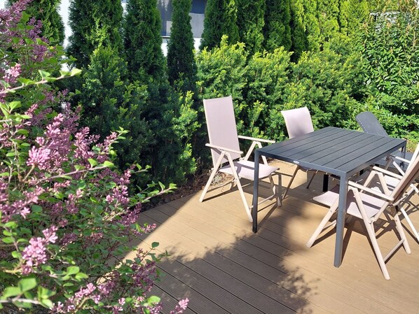 Een terras buiten met een tafel en stoelen, omringd door weelderige begroeiing en bloeiende planten.