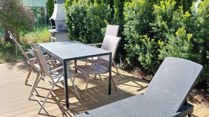 Eine Terrasse im Freien mit einem Metalltisch, Stühlen, einer Lounge-Liege und einem Grill.