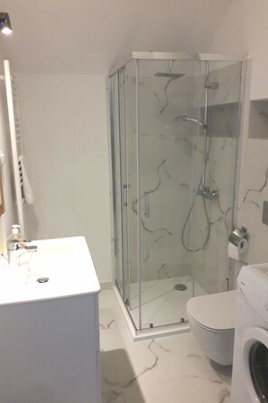 Een moderne badkamer met een glazen douchecabine, een wit wastafelmeubel en een toilet.