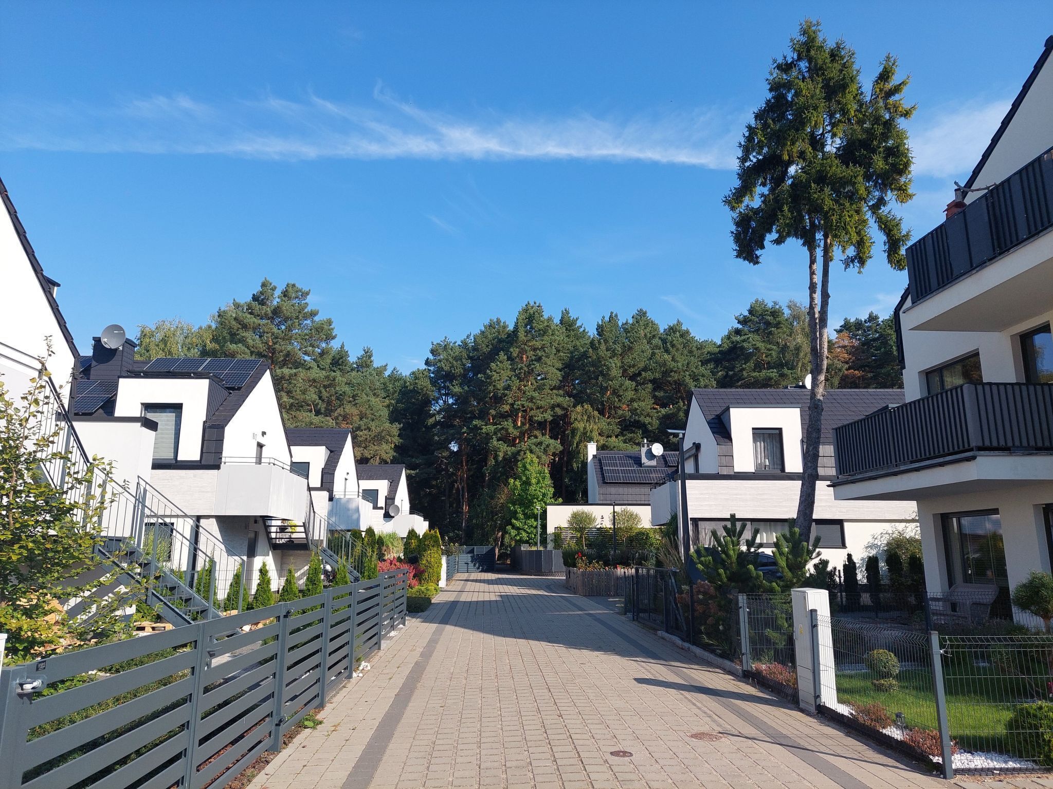 Rua residencial com casas modernas, calçada pavimentada e céu azul límpido.