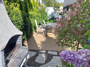 Een terras met een barbecue, buitenmeubels en een tuin met bloeiende planten.