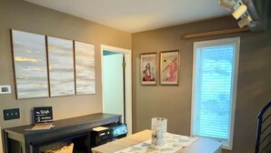 Un comedor con una mesa y bancos de madera, una pequeña cocina con microondas, y obras de arte en las paredes.