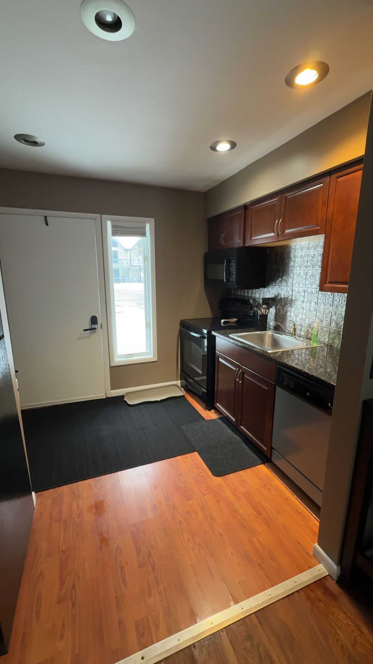 A kitchen with wooden cabinets, a microwave, a dishwasher, and a window with a view of the outside.