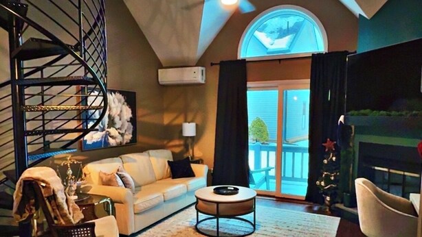 Un salón espacioso con techo alto, una escalera de caracol, un ventanal grande y una chimenea.