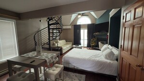 Un dormitorio con cama, escritorio con silla, sofá, escalera de caracol y chimenea.