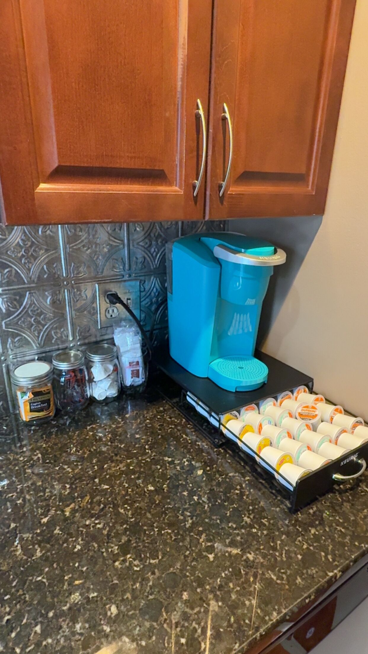 A kitchen with wooden cabinets, a coffee maker, jars, and a tray of packaged food items.