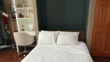 A neatly made bed in a room with a wooden floor, a white chair, and a wooden door.