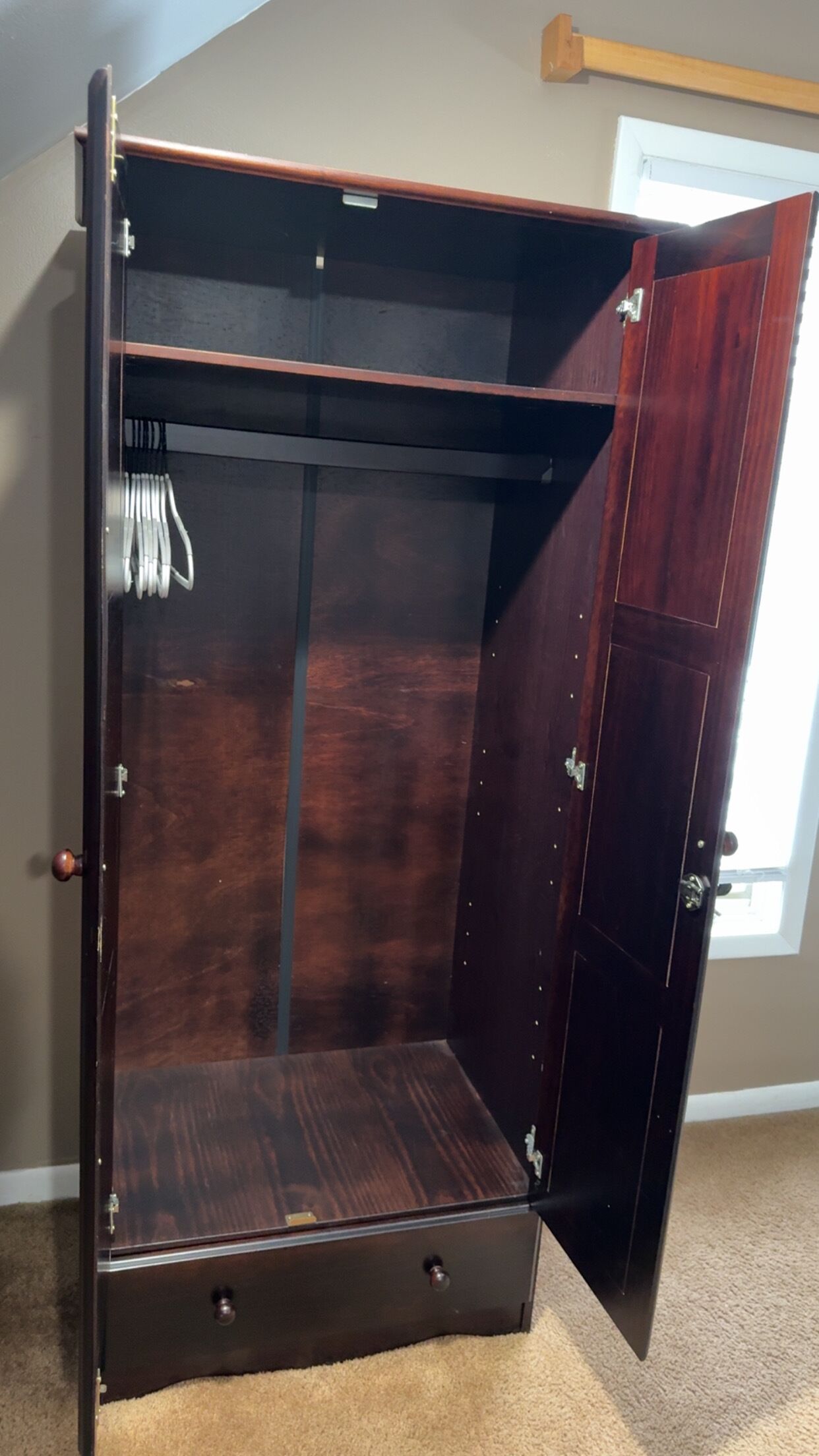 A dark wooden wardrobe with a mirrored interior, a small drawer, and a hanging rod.