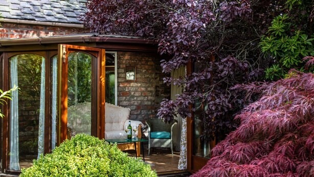 Une pièce chaleureuse avec une porte vitrée donnant sur un jardin, un canapé et une table sur laquelle se trouvent une bouteille et des verres.