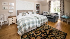 Une chambre avec deux lits, un canapé, une chaise, une bibliothèque et une fenêtre avec des rideaux.