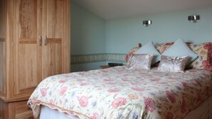 Quarto com um amplo guarda-roupa de madeira, colcha de cama com padrão floral e duas luminárias fixadas na parede.