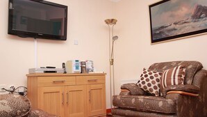 Uma sala de estar com televisão de tela plana, um sofá, uma poltrona estampada, um armário de madeira e um quadro.
