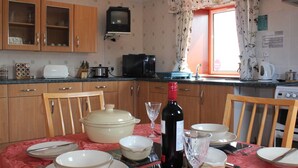 Cozinha com armários de madeira, micro-ondas, torradeira e mesa de jantar posta com pratos, tigelas e uma garrafa de vinho.