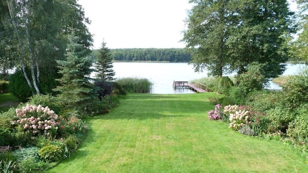 A well-maintained lawn with a dock extending into a lake, surrounded by dense trees and shrubs. - Glücksurlaub mit Hund am See by Interhome (Rózansko)