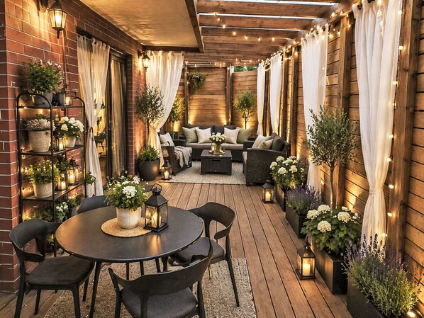 An outdoor patio with a round table, chairs, a sofa, and potted plants.