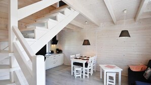 Un interior moderno con una escalera que lleva a una habitación loft, un comedor con mobiliario blanco y un sofá negro.