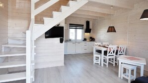 Un interior moderno con una escalera de madera, una cocina con armarios blancos y un comedor con mobiliario blanco.