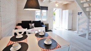 Una habitación acogedora con una mesa blanca dispuesta para dos personas, una lámpara negra y una escalera a la derecha.