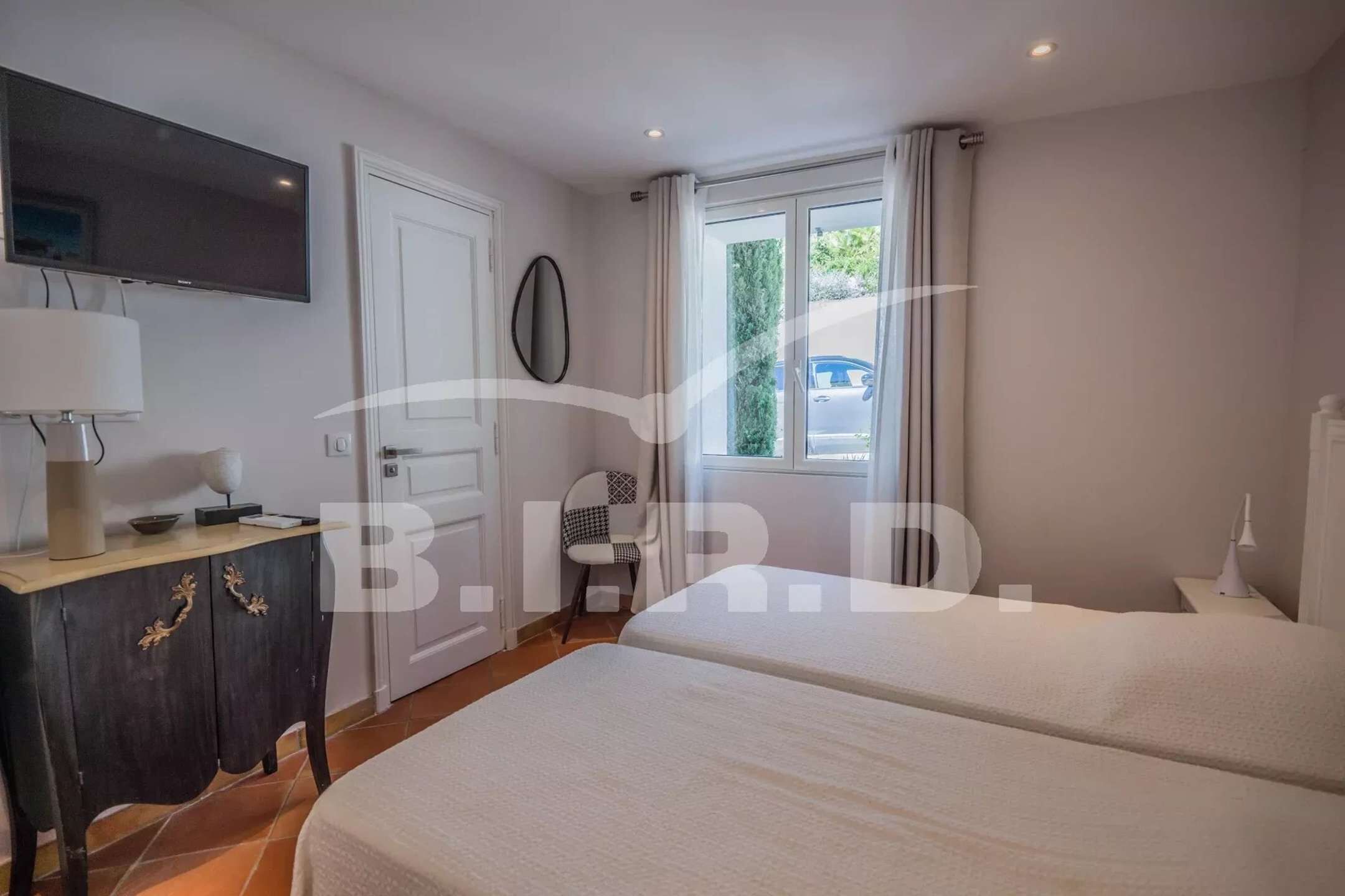 A hotel room with a bed, a desk with a lamp, a chair, a TV, and a window with curtains.