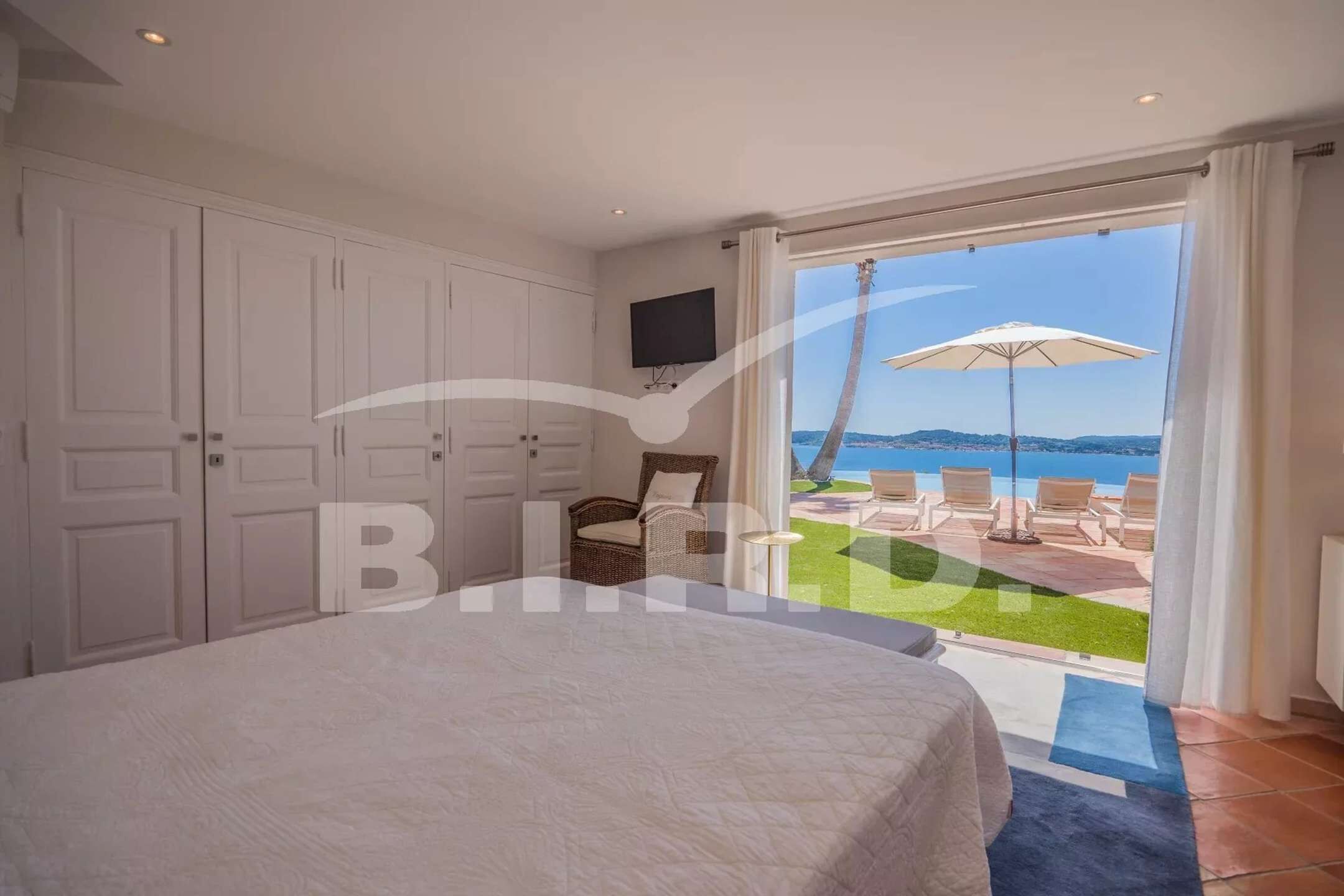 A bedroom with a bed, a television, and a balcony with a view of the sea.