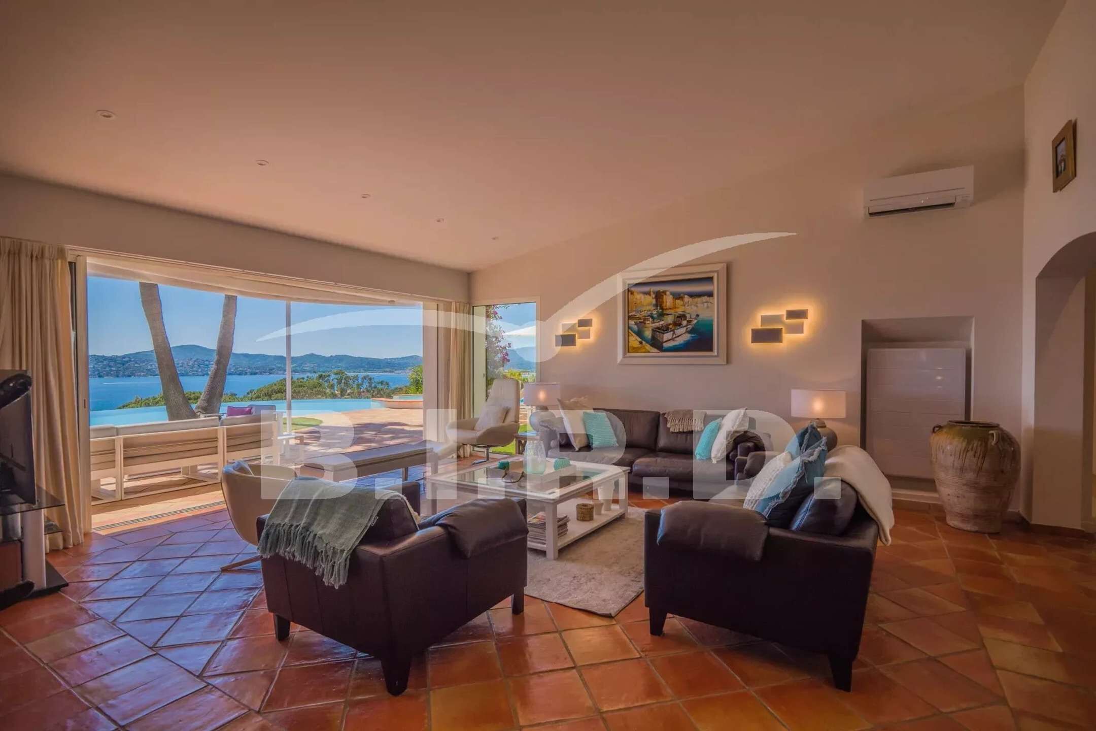 A spacious living room with a large window offering a view of the sea and mountains, a sofa set, a coffee table, and a large vase.