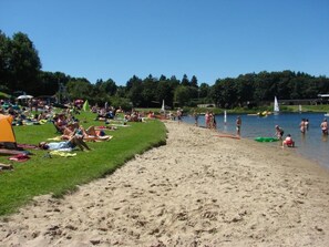 Una playa arenosa con gente tomando el sol y nadando.