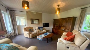 Ein geräumiges Wohnzimmer mit Ledersofas, einem Holztisch und einem an der Wand befestigten Fernseher.