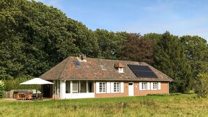 Ein eingeschossiges Backsteinhhaus mit geneigtem Dach, einer kleinen angebauten Garage und einer Terrasse mit Sitzgelegenheiten.