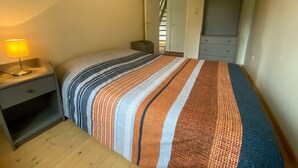 Ein Schlafzimmer mit einem Bett, einem Nachttisch mit Lampe, einem Kleiderschrank und einer Tür zu einer Treppe.
