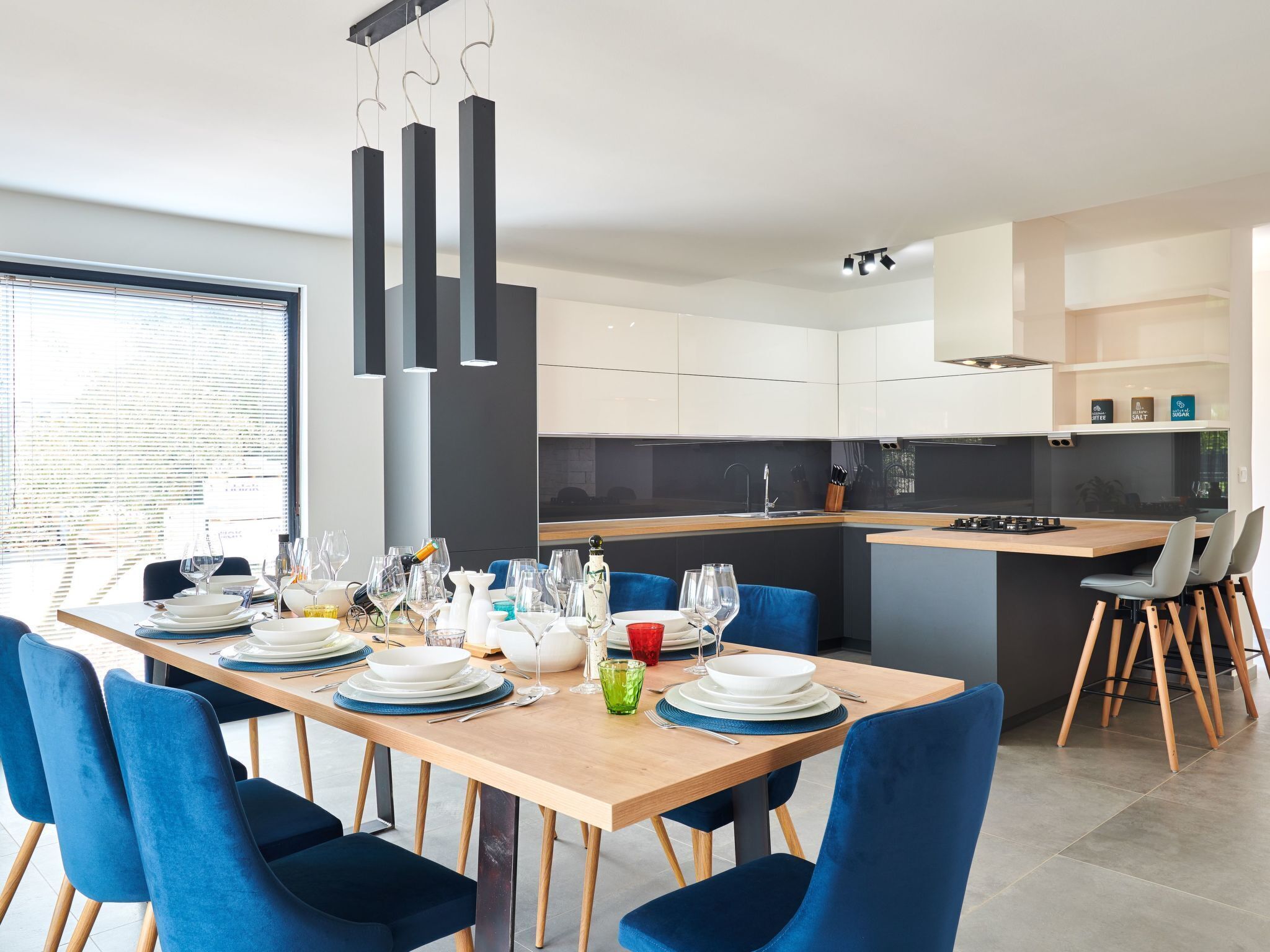 A modern dining area with a wooden table set for six, blue chairs, and a kitchen in the background.