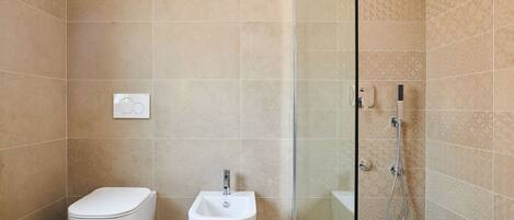 A modern bathroom with a toilet, bidet, and glass-enclosed shower area.