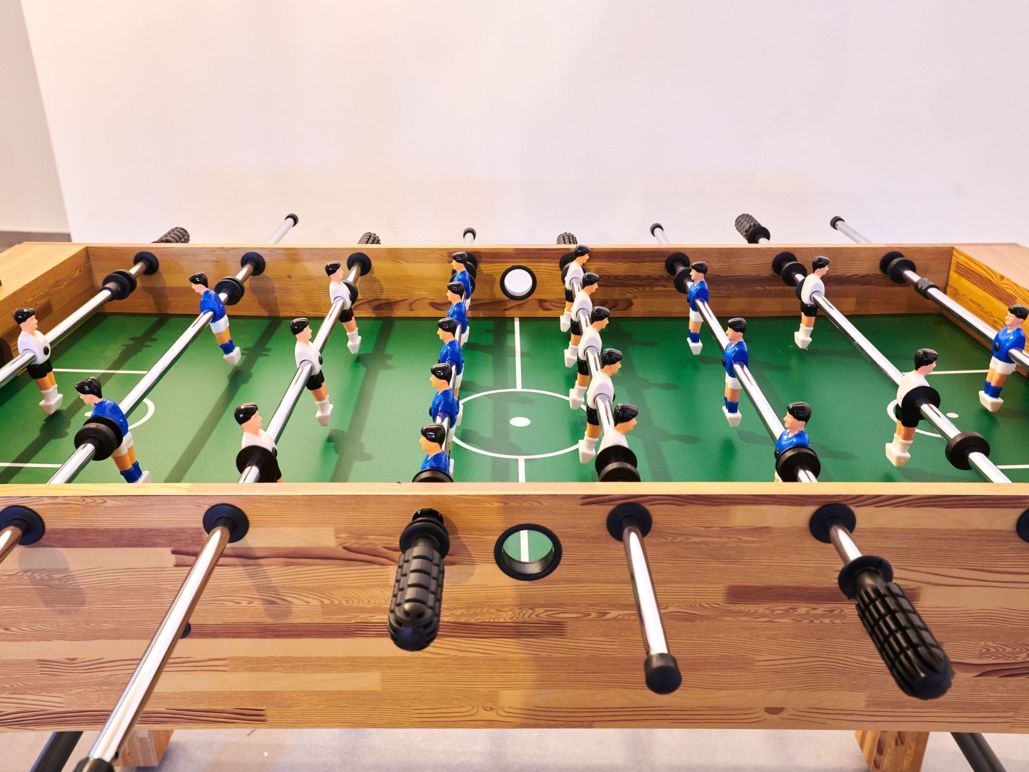 A wooden foosball table with players in blue and white uniforms.