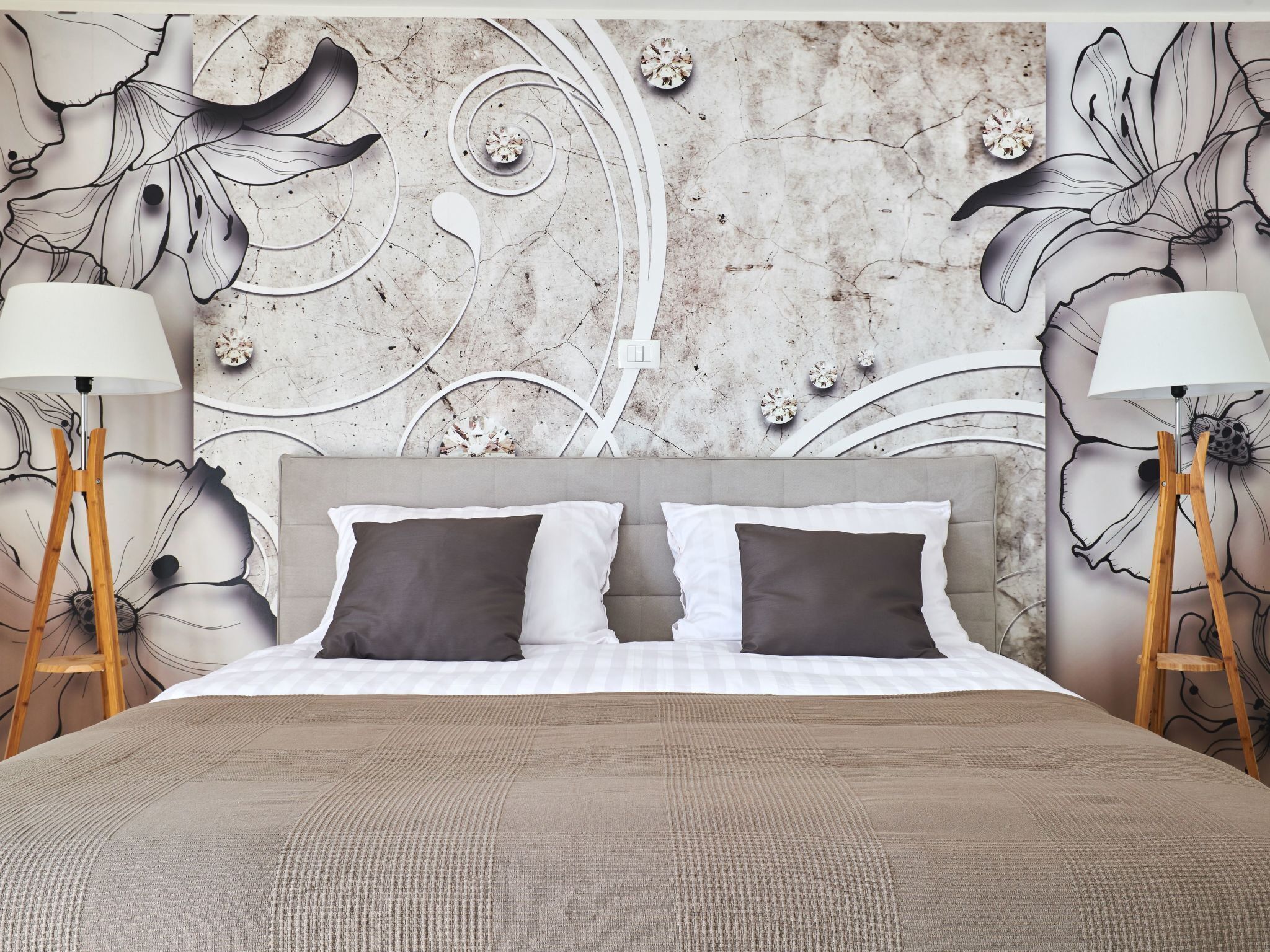 Une chambre d’hôtel avec un grand lit, deux lampes de chevet et un mur décoratif orné de motifs floraux.
