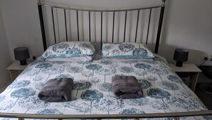 A single bed with a metal frame, two pillows with a floral pattern, two bedside lamps, and two folded towels on the bed. - Velvet Cottage by Interhome (Pentrefelin)