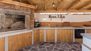A rustic kitchen with a stone floor, wooden cabinets, a brick oven, and a hanging light fixture. - Villa Deni by Interhome (Buje)