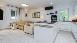 A modern living room with a sofa, a coffee table, and a kitchen area with a TV and a window. - Villa Deni by Interhome (Buje)