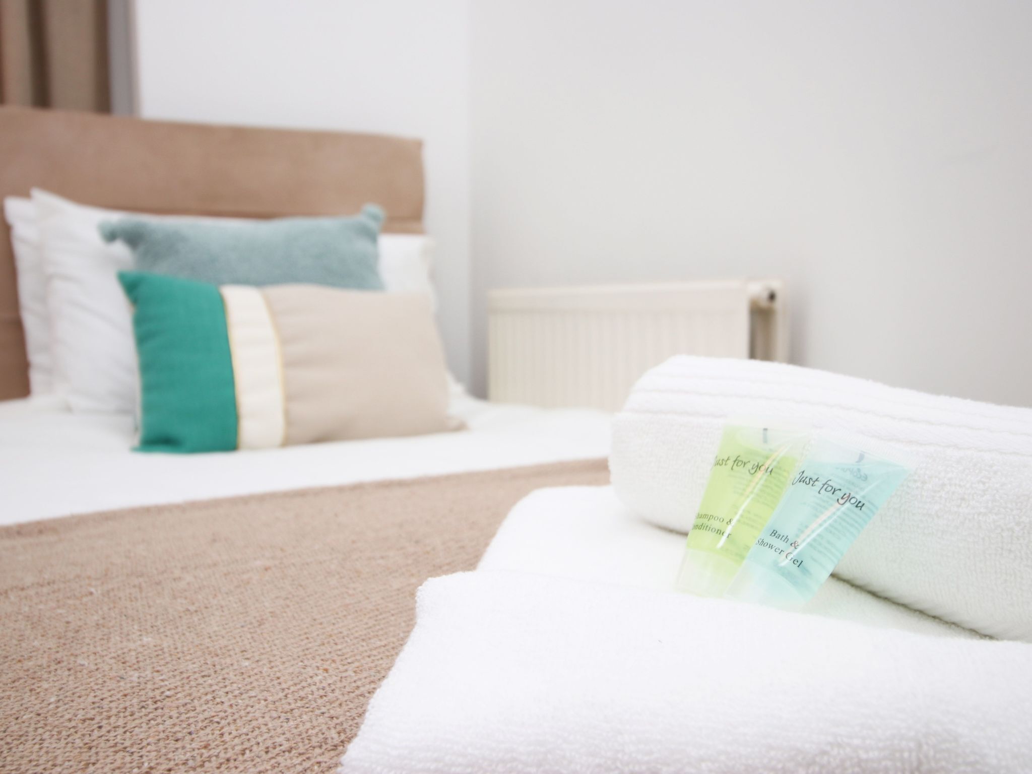 A neatly made bed with a white and green towel, a headboard, and a radiator in the background.