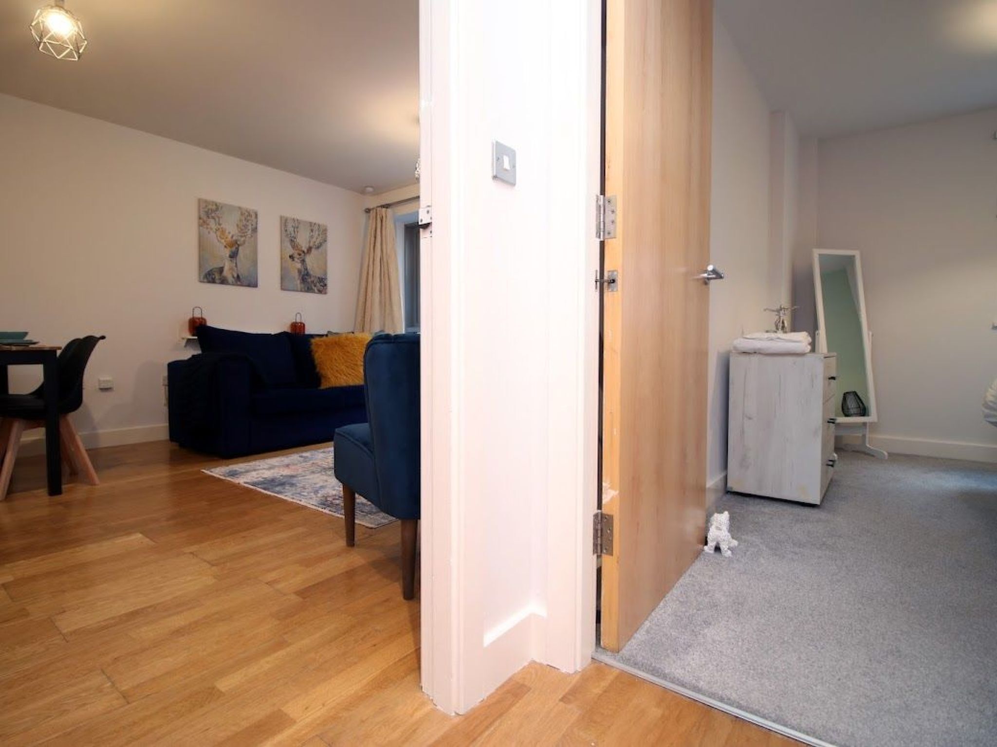 Un appartement moderne avec un plancher en bois, un canapé bleu foncé, une petite table à manger et une armoire blanche.