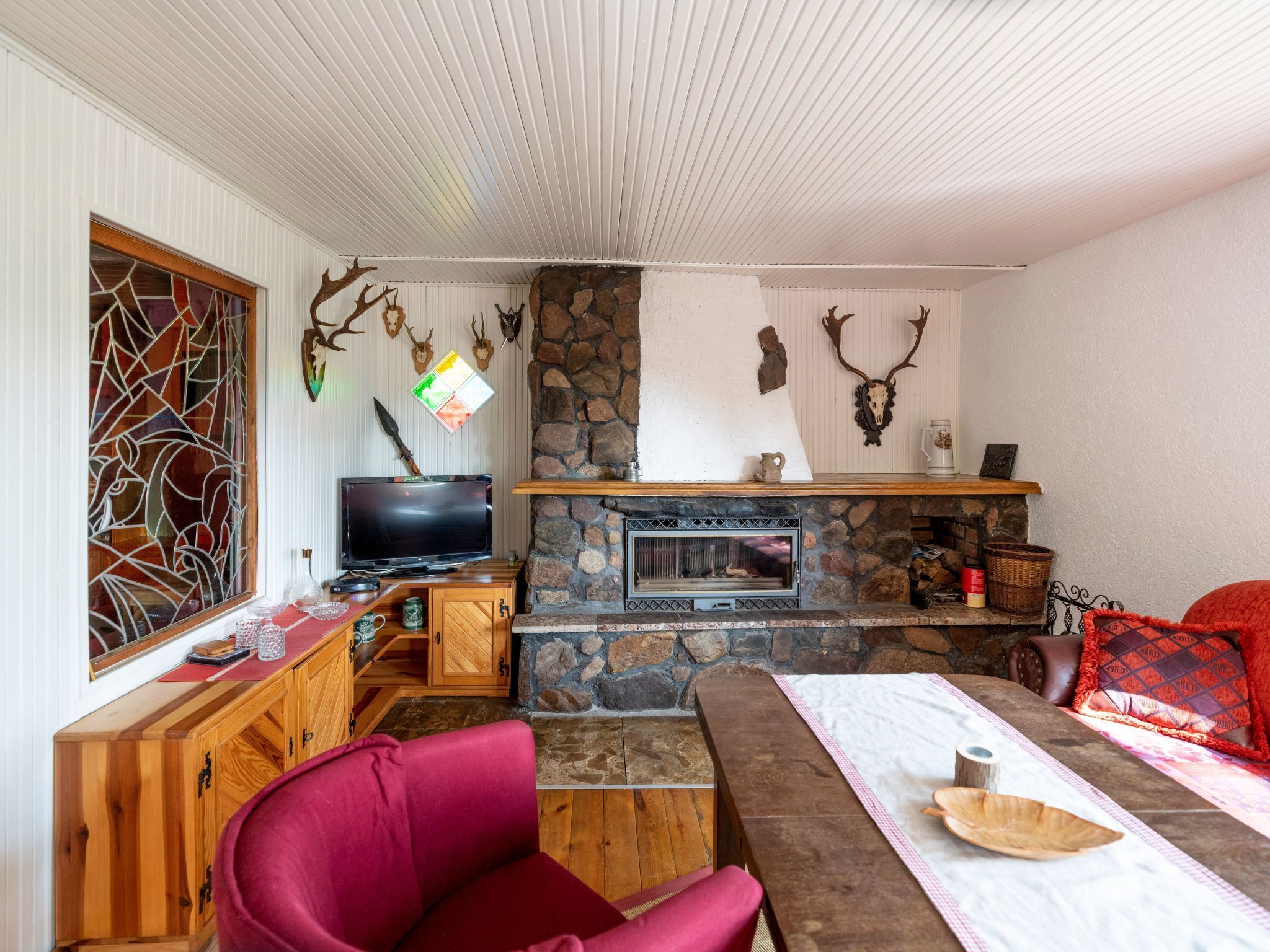 A cozy living room with a stone fireplace, wooden furniture, and antler decorations.