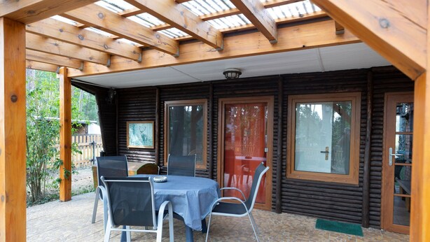 Uma cabana de madeira com varanda coberta, uma mesa de jantar com cadeiras e uma janela grande.