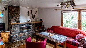 A cozy living room with a stone fireplace, a red sofa, and a television on a wooden cabinet. - Blockhütte Rudolf by Interhome (Zernitz)