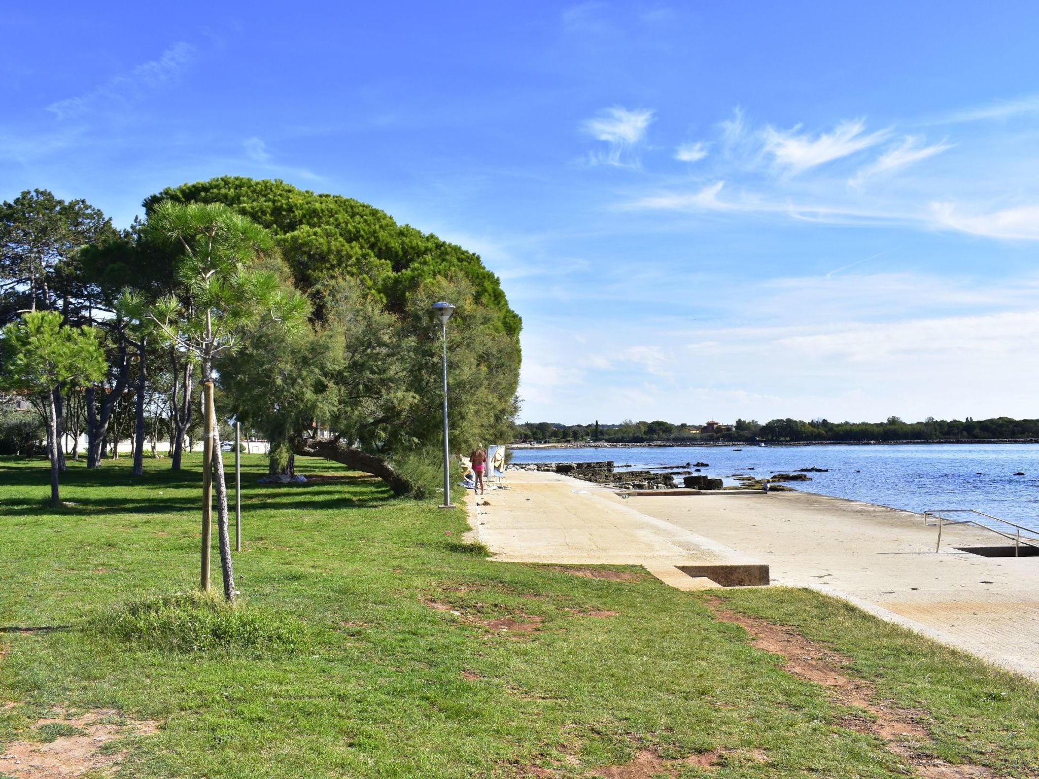 Un parque con un sendero, árboles y una playa bajo un cielo despejado.