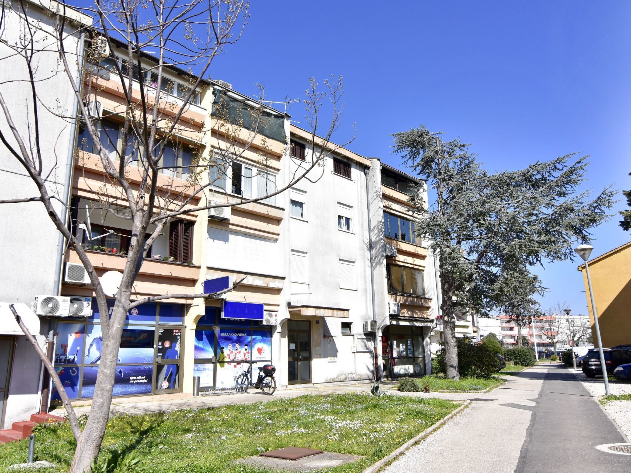 A multi-story building with a ground-floor commercial space, a bicycle parked outside, and a clear sky.