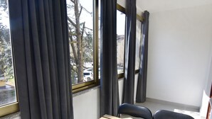 Une pièce avec une table en bois mise pour le petit-déjeuner, une fenêtre avec des rideaux et une vue sur les arbres et les voitures garées à l’extérieur.