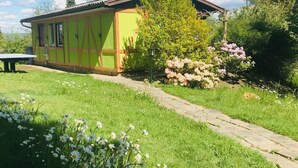 Ein Haus mit grüner Fassade und einem sichtbaren Garten mit Blumen und einem Weg.