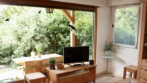 Ein gemütliches Wohnzimmer mit einem Holztv-Schrank, einem Esstisch und Stühlen. Ein großes Fenster bietet Blick auf grüne Landschaft.