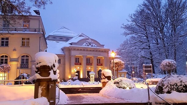 Ein schneebedecktes Gebäude mit Stufen, umgeben von mit Schnee beladenen Bäumen und einem klaren Himmel.