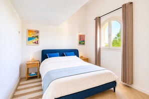 A bedroom with a bed, wooden nightstands, a window with curtains, and two wall-mounted pictures. - Semi-Detached House with Pool – 3 Bedrooms (GRIMAUD)
